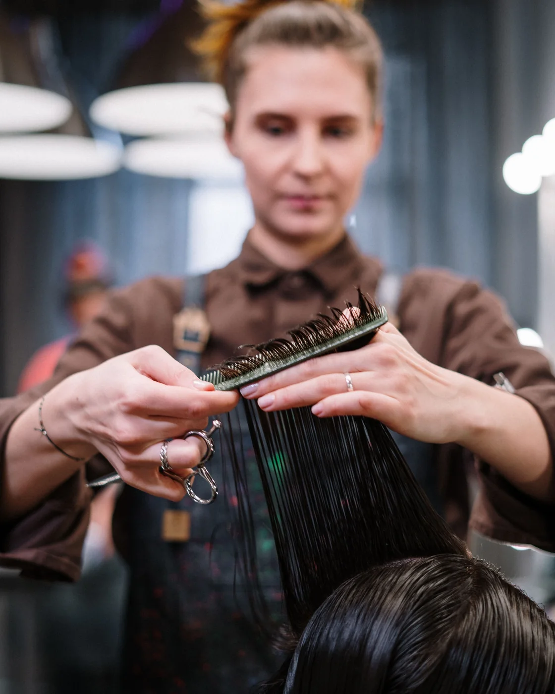 Een kapper knipt donker haar met een schaar en borstel.